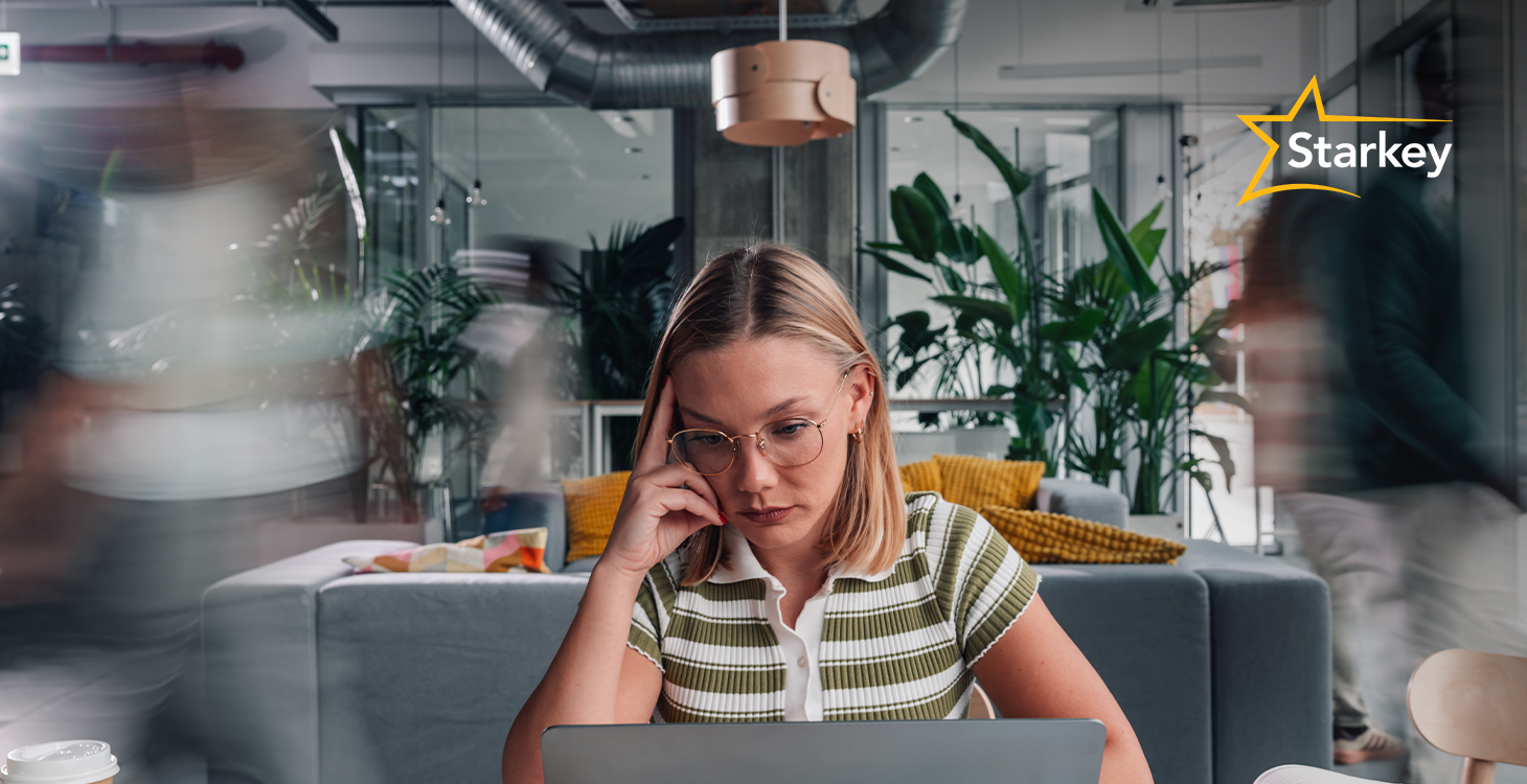 Image of woman in the office looking at computer as people rush past her